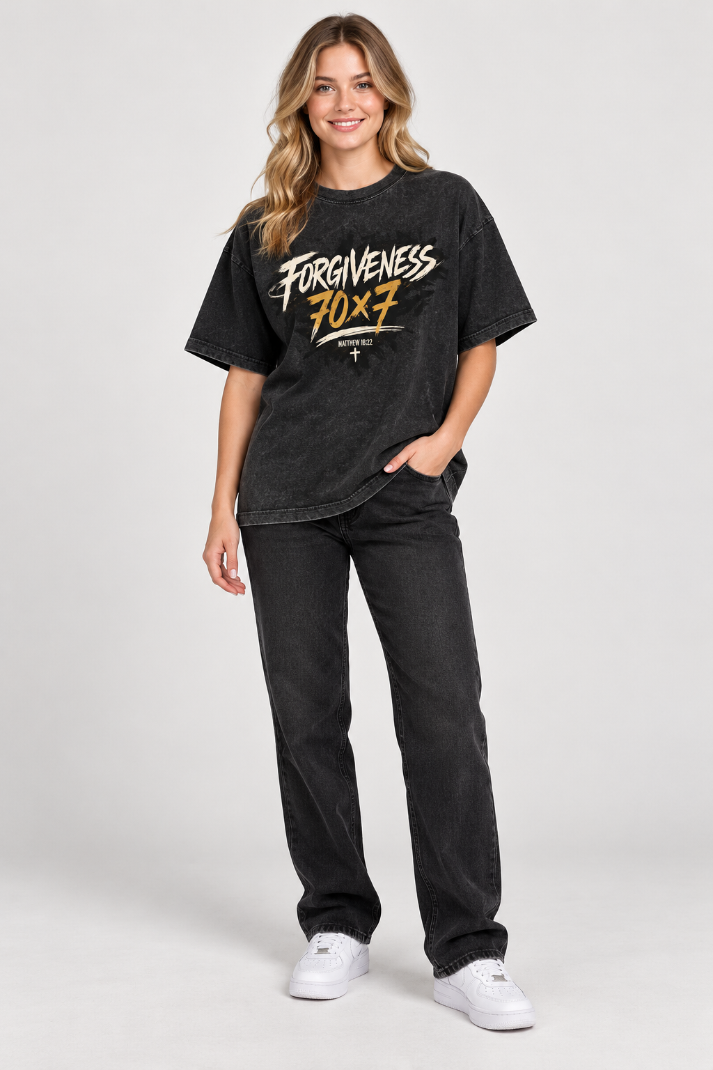 Smiling female model wearing Black Forgiveness 70x7 tee with original artwork, black jeans