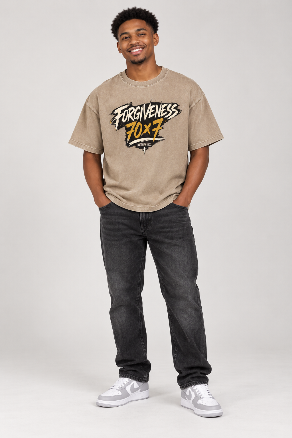 Smiling male model wearing Khaki Forgiveness 70x7 tee with original artwork, dark jeans